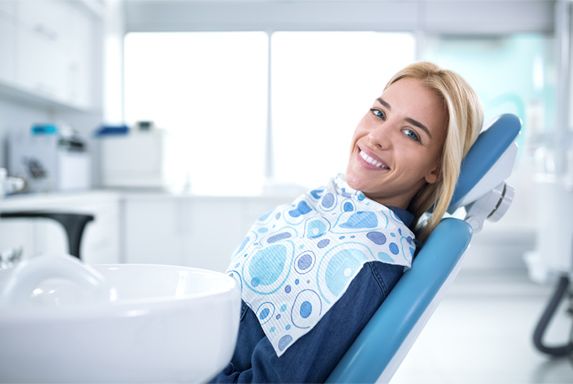 smiling woman waits in dentist chair for dental work 