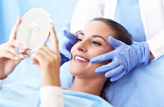 young woman smiling into mirror with dentist holding her head
